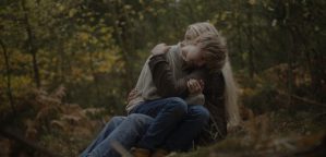 Still image showing a child hugging a girl in the forest.